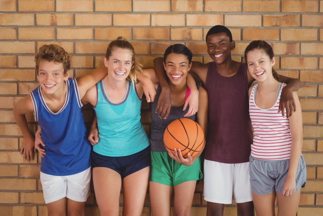 Fünf Jugendliche die mit einem Basketball an einer Wand lehnen.