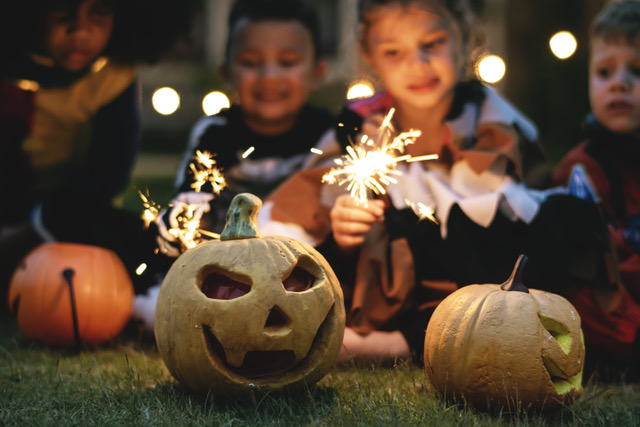 Kinder mit Wunderkerzen hinter geschnitzten Halloween-Kürbissen.