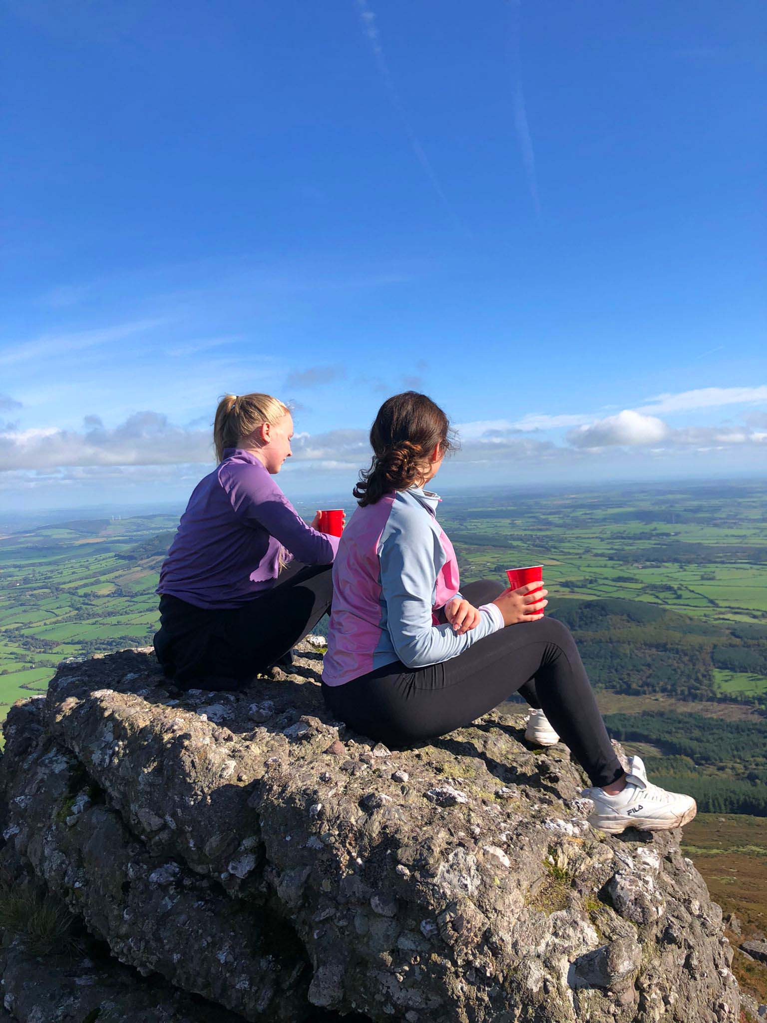 Zwei Teilnehmerinnen sitzen auf einem Berg in Irland und genießen die Aussicht